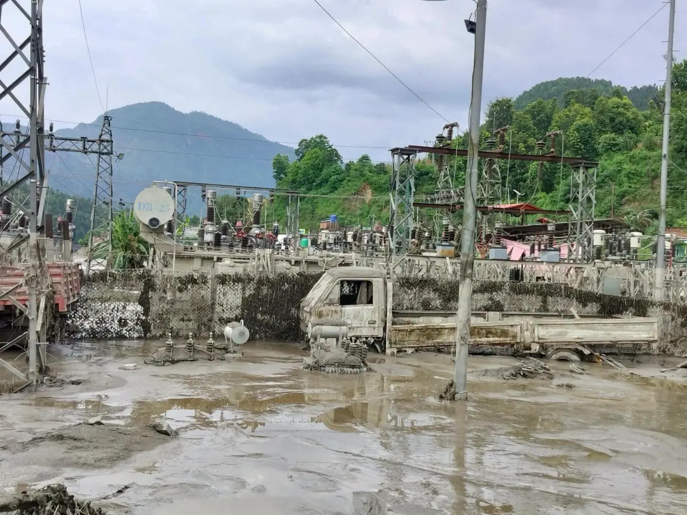 A substation in the Rasuwagadhi corridor buried in mud, with a truck submerged to its cab and transmission towers still standing behind it